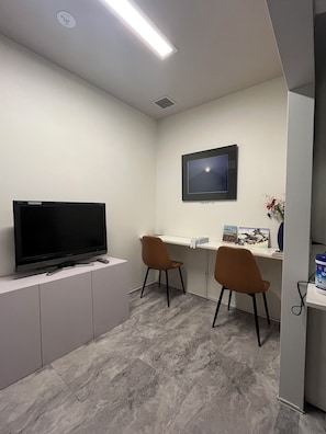 A modern office space with a flat-screen TV mounted on the wall, two brown chairs, a white desk, and a grey cabinet.