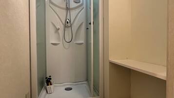 A compact shower stall with a glass door, a small shelf, and a basket.