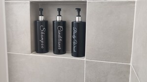 A bathroom with three black bottles labeled "Shampoo," "Conditioner," and "Body Wash" in a tiled wall shelf.