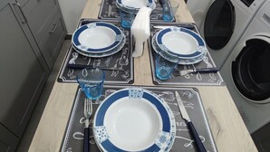Uma mesa de jantar posta com pratos azuis e brancos, talheres e copos, com uma máquina de lavar e armários ao fundo.