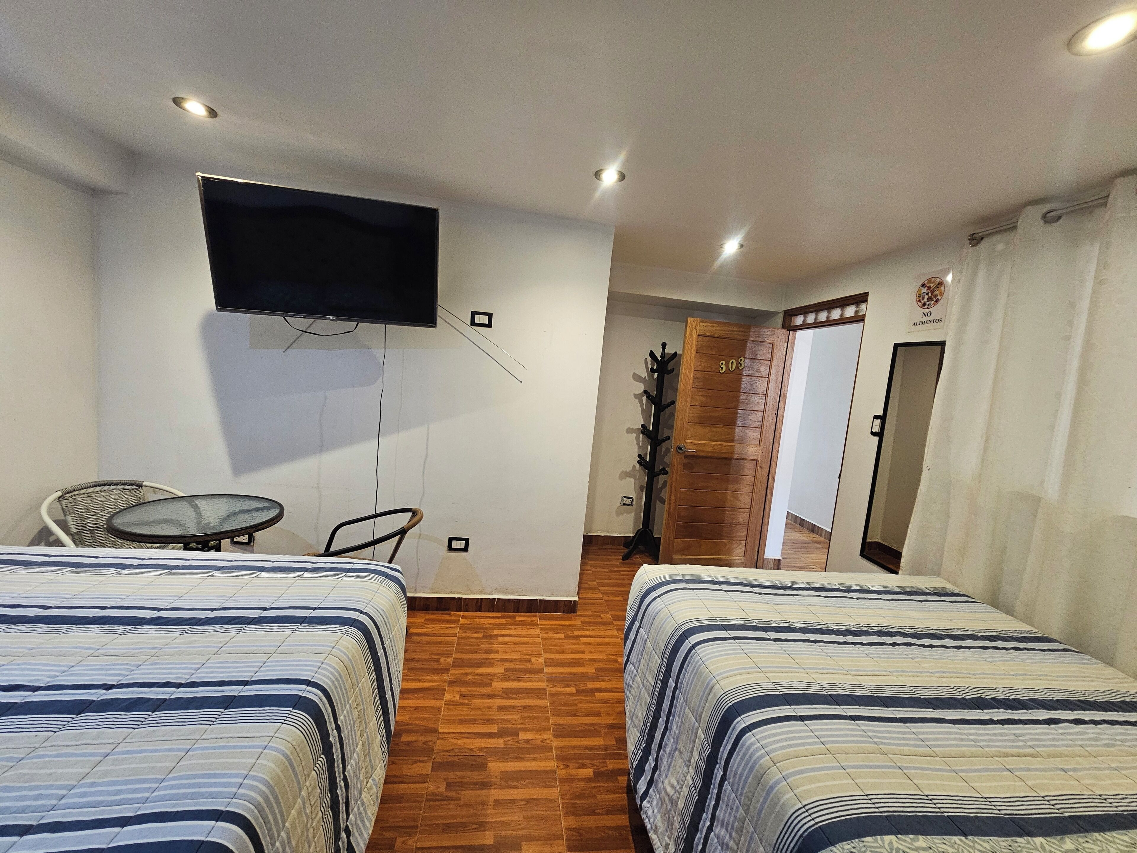 A hotel room with two beds, a TV mounted on the wall, a coat rack, and a door with a number.