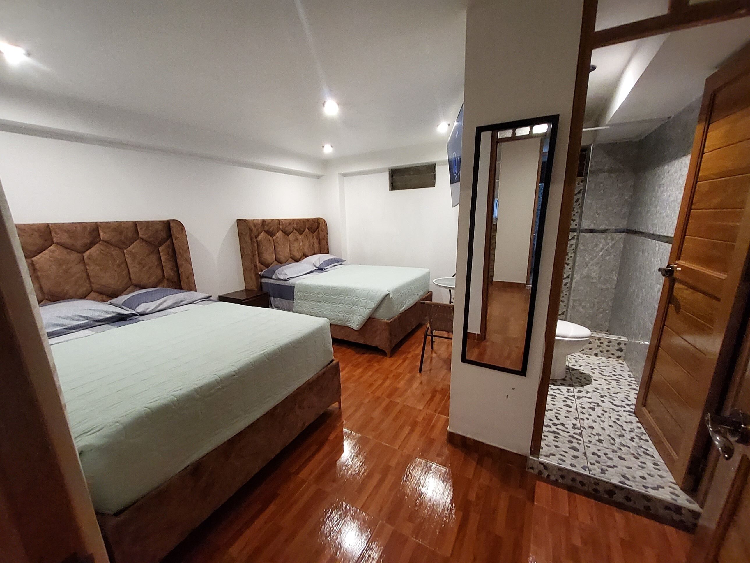 A hotel room with two beds, a small table, and a shower area.