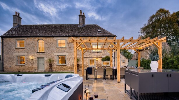 Edificio de piedra con una pérgola de madera, mobiliario exterior y un jacuzzi.