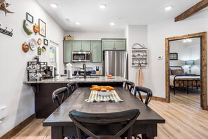 Una cocina moderna con zona de comedor, que cuenta con una isla central, electrodomésticos de acero inoxidable y una variedad de utensilios de cocina exhibidos en las paredes.