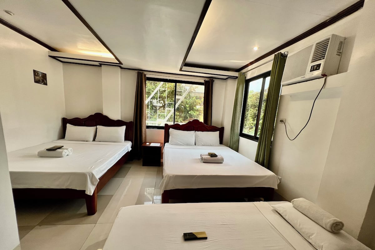 Quarto de hotel com duas camas de solteiro, uma janela grande e um aparelho de ar condicionado.