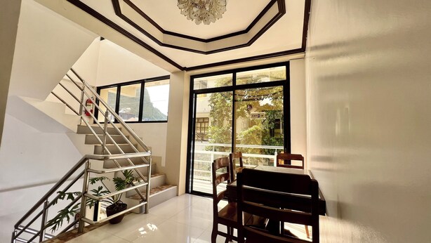 A modern interior with a staircase, a chandelier, and a view through large windows. - Alocasia El Nido (El Nido)