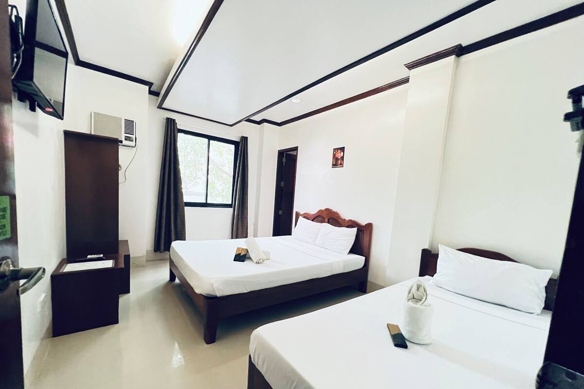 Quarto de hotel com duas camas, televisão fixada na parede e janela com cortinas.