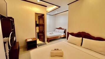 Une chambre d’hôtel avec un grand lit, une tête de lit en bois, une table de chevet et une petite commode. Une porte donne accès à une salle de bain et à un placard.