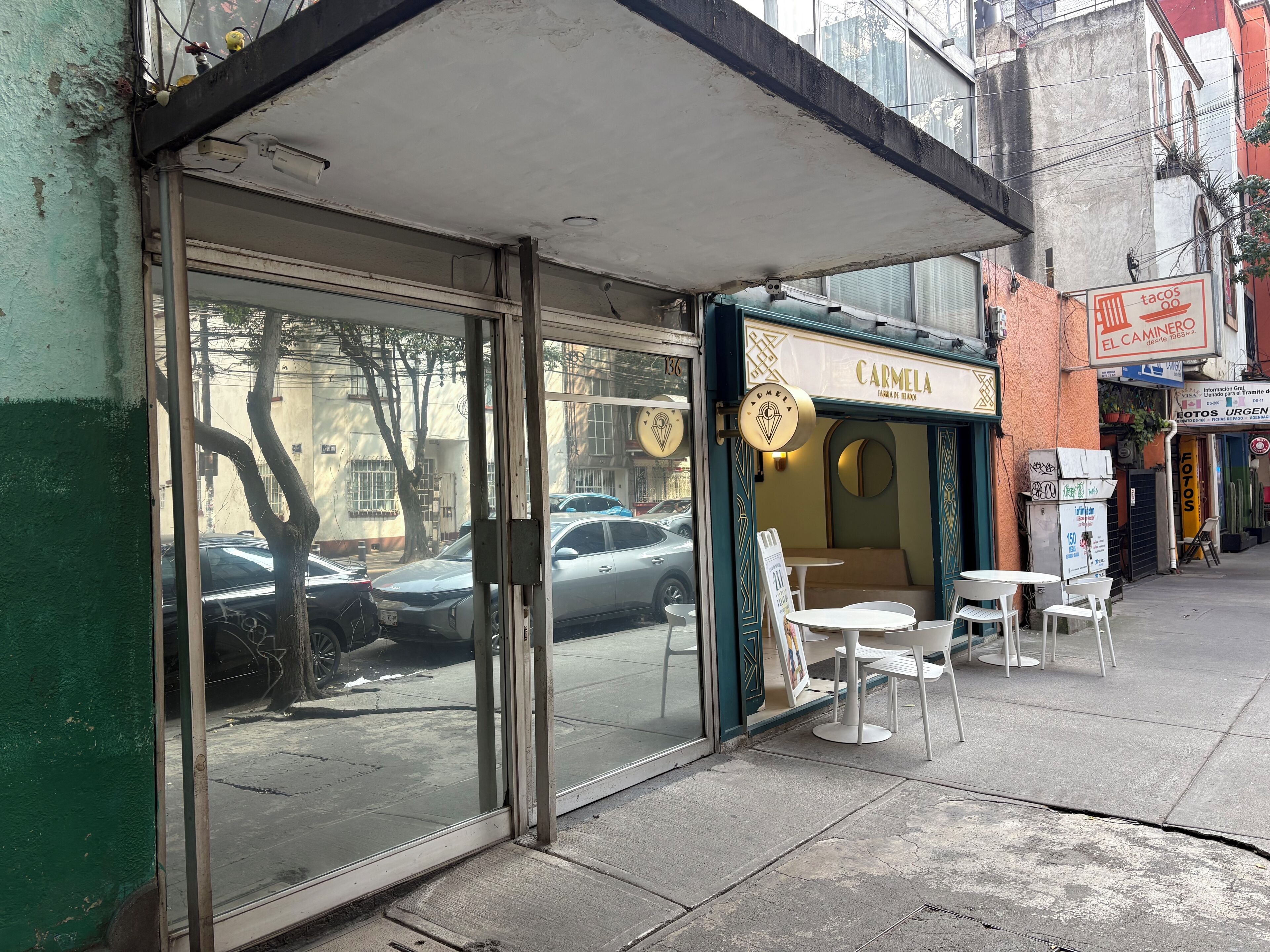 Una fachada con puerta de vidrio y un pequeño espacio al aire libre con sillas blancas.