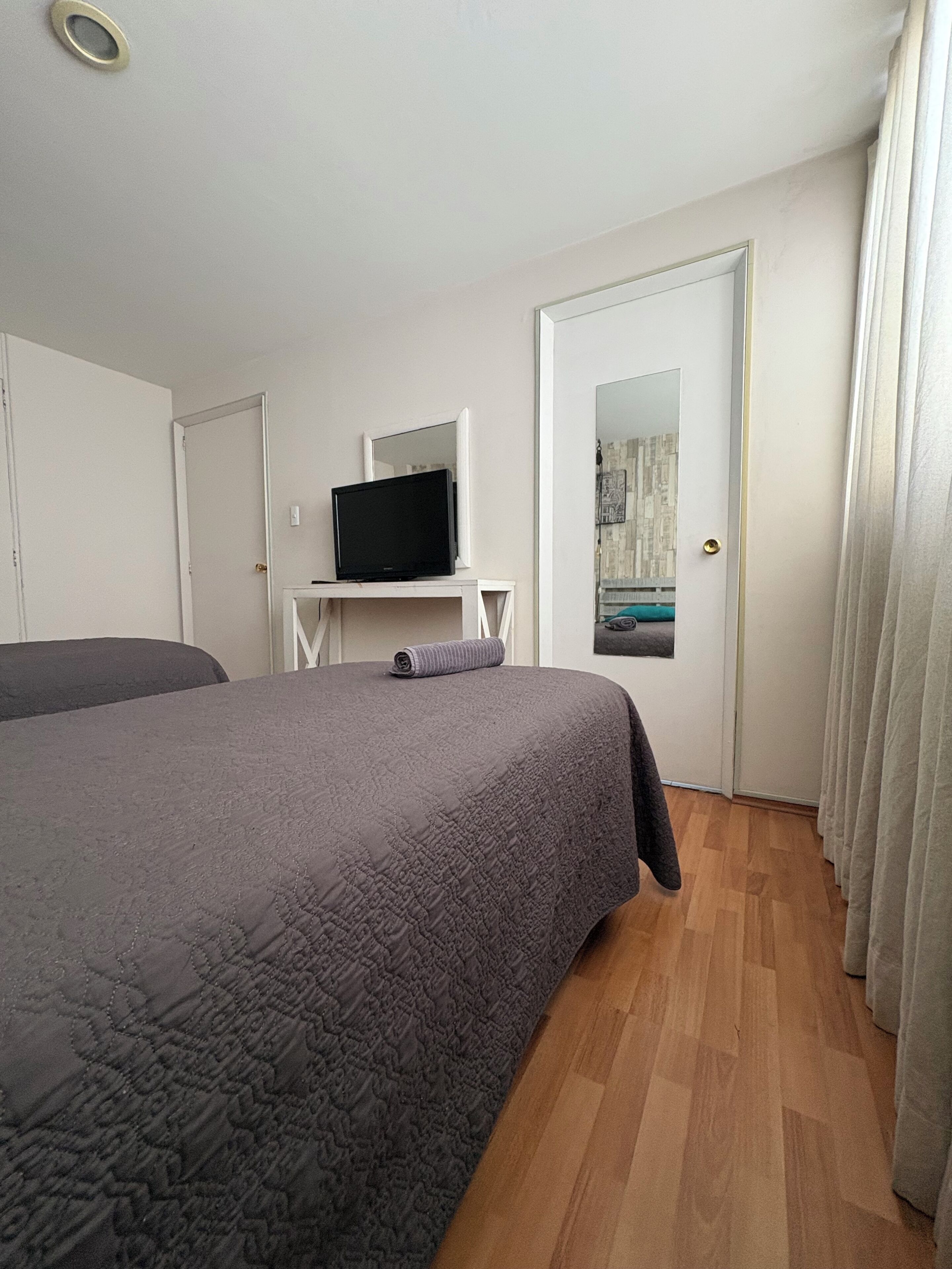 Une chambre à coucher avec un grand lit, un téléviseur posé sur un meuble et une porte dotée d’un miroir.