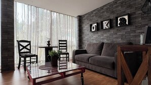 A modern living room with a wooden floor, a grey sofa, a glass coffee table, and a brick accent wall with framed letters. - 5 minutes walking distance from Angel Reforma (Ciudad de México)
