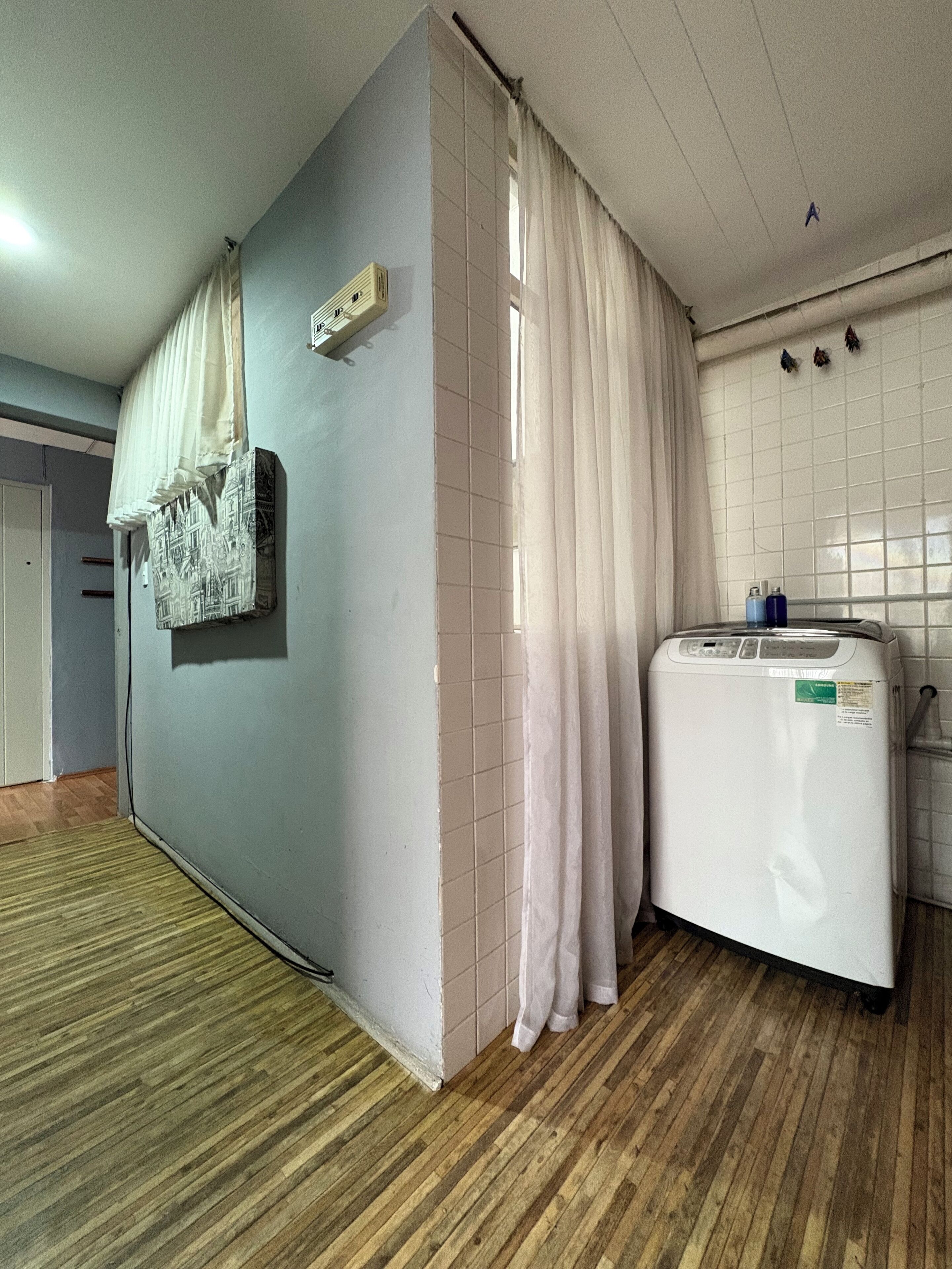 A room with a washing machine, a tiled wall, and a wooden floor.