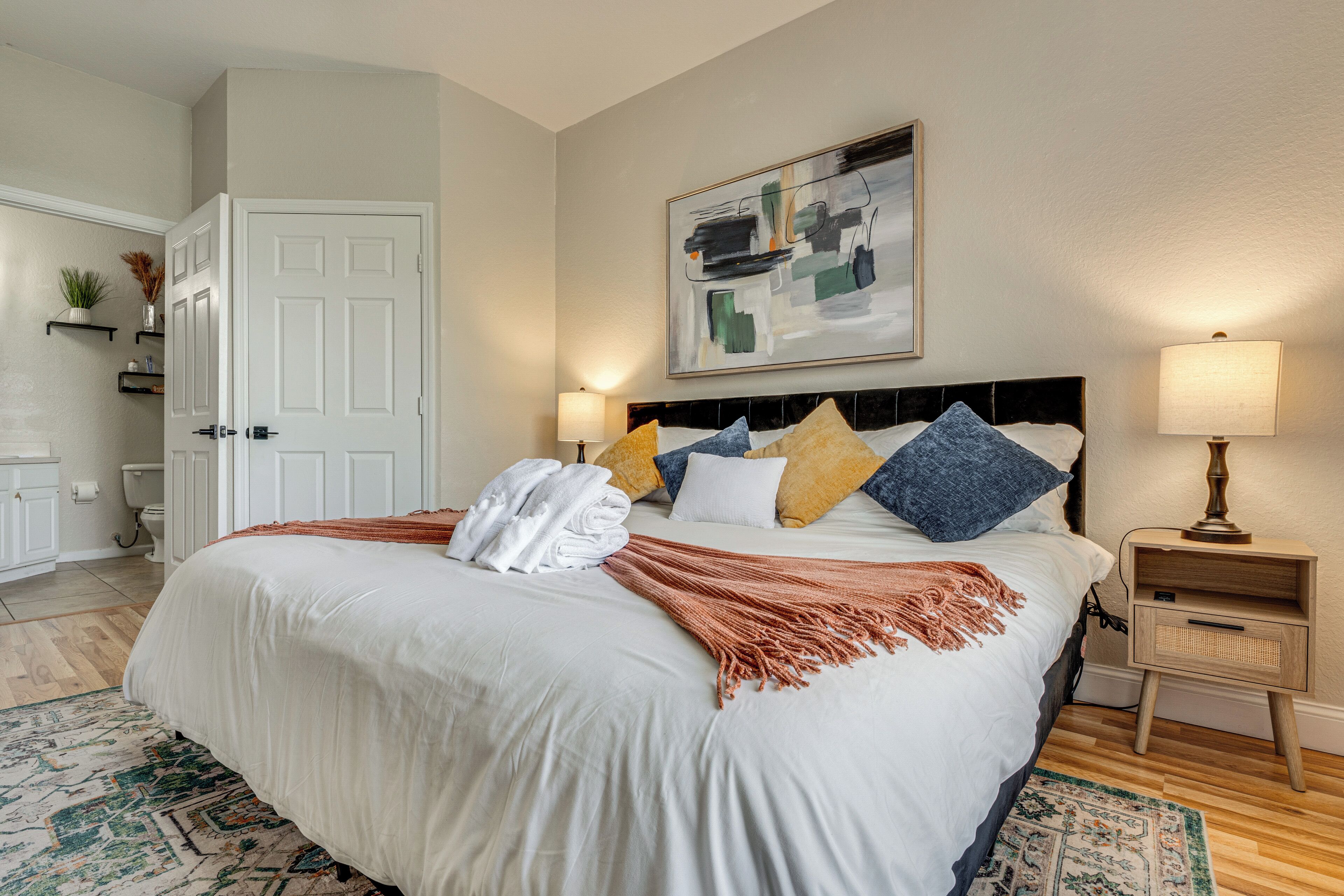 A neatly arranged bedroom with a large bed, bedside lamps, a headboard, and a painting on the wall.
