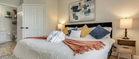 A neatly arranged bedroom with a large bed, bedside lamps, a headboard, and a painting on the wall.