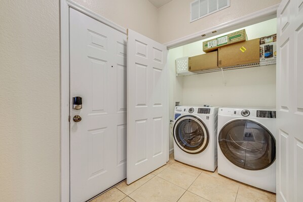A laundry room with two front-loading washing machines, a shelf above with boxes, and a white door. - 4 Mi to Disney: Family-Friendly Resort Getaway! (Kissimmee)