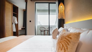 A hotel room with a large bed, a wardrobe, a balcony with chairs, and a hanging light fixture. - NOVO CANGGU (Pererenan)