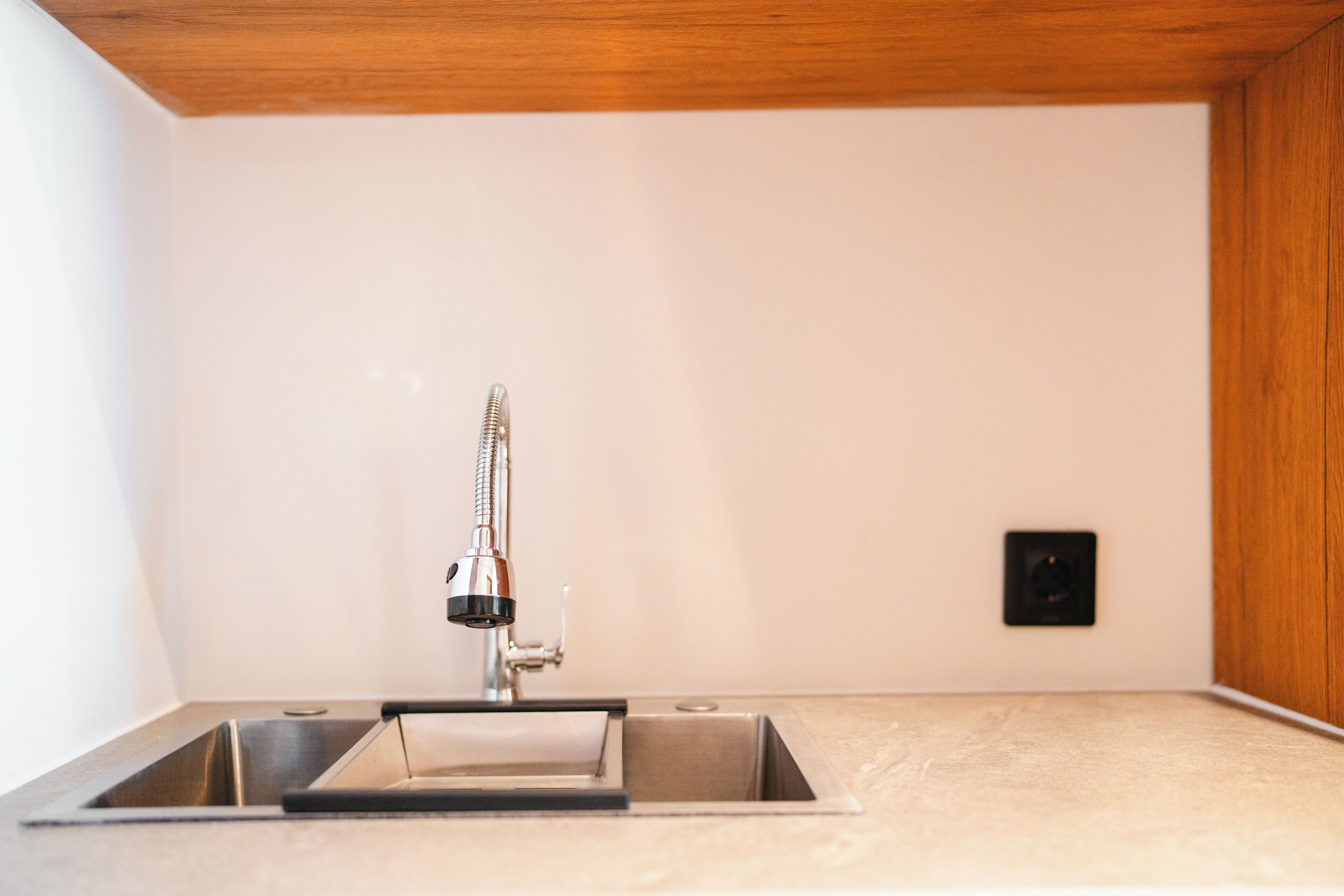 Una cocina con un lavamanos de acero inoxidable, techo de madera y pared blanca.
