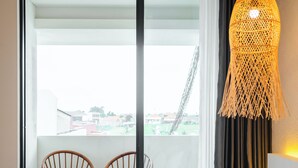 A hotel room with a bed, a large window with a view, two wooden chairs, and a hanging light fixture. - NOVO CANGGU (Pererenan)