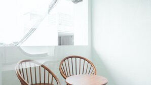 A modern room with two wooden chairs and a small table, large windows, and a view of a building outside. - NOVO CANGGU (Pererenan)