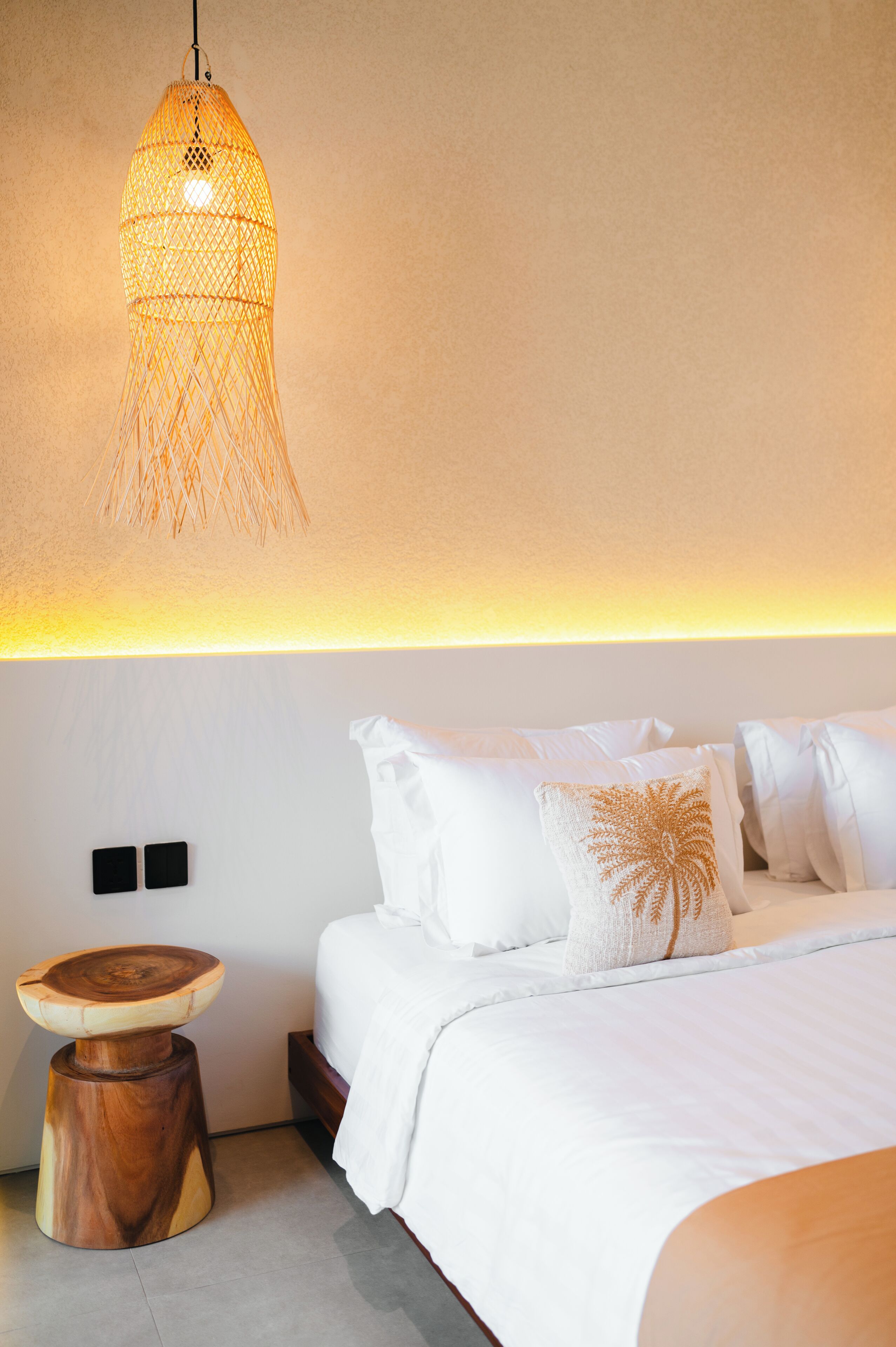 A bedroom with a bed, white bedding, a wooden side table, and a hanging light fixture.