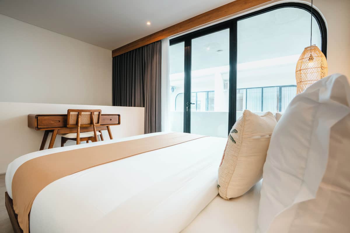 A modern hotel room with a large bed, a wooden desk, and a view of the balcony.