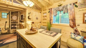 Un intérieur en bois avec une table à manger, des chaises, une guitare et une fenêtre avec des rideaux.