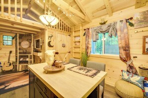 Un interior de madera con una mesa de comedor, sillas, una guitarra y una ventana con cortinas.