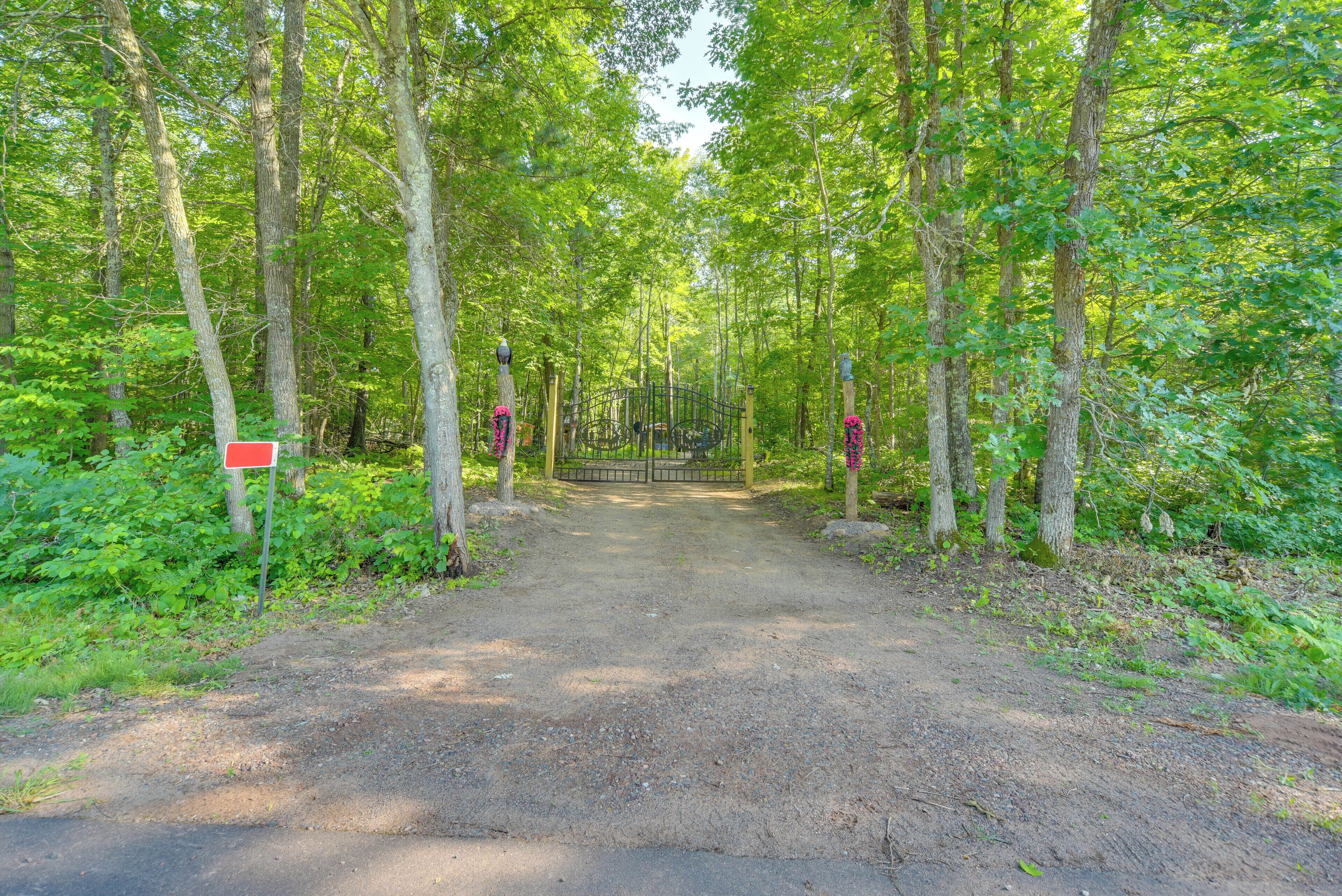 A forested path leading to a gated area with a red sign on the left.