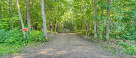 A forested path leading to a gated area with a red sign on the left.