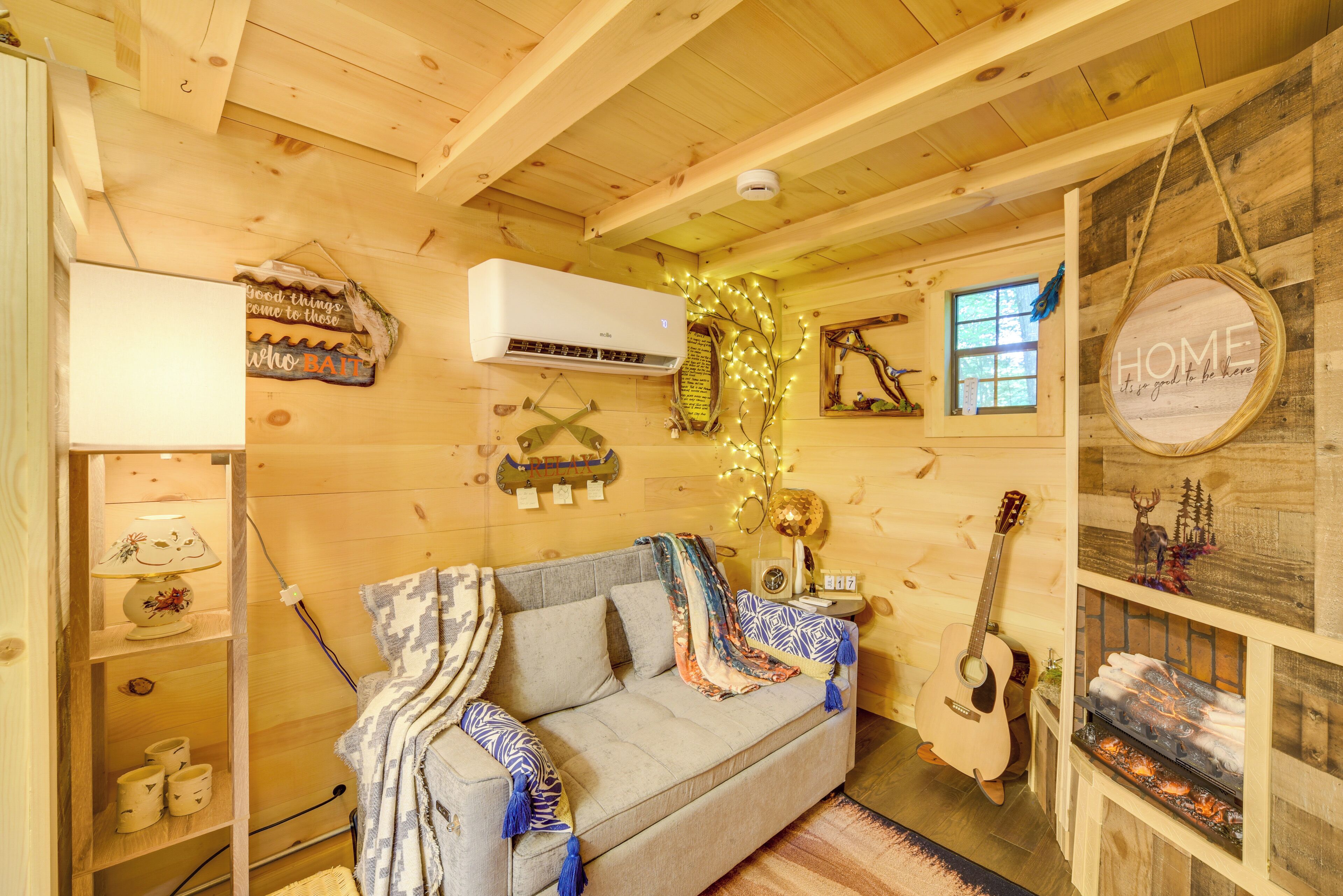 L’intérieur chaleureux d  ’un chalet avec un plafond en bois, un canapé recouvert de couvertures, une guitare, une cheminée et un climatiseur fixé au mur.