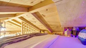 Une pièce chaleureuse avec un lit, des poutres en bois et un plafond éclairé de lumières violettes.