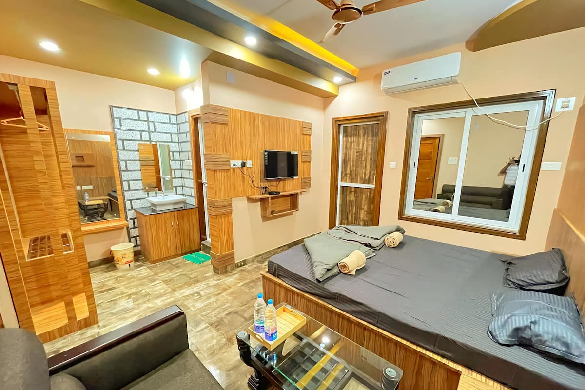 Habitación de hotel pequeña con cama, un rincón de descanso, televisión, espejo y baño.