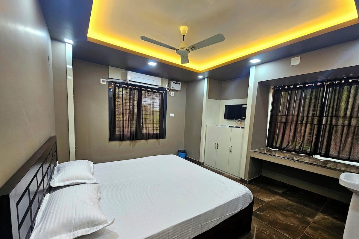 Un dormitorio con cama, ventilador de techo, unidad de aire acondicionado, armario, televisión y ventana con cortinas.