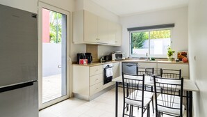 A compact kitchen with a refrigerator, microwave, coffee maker, and a dining area with a table and chairs. - GuestReady - Exquisite stay with sea views (Calheta)