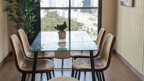 A dining area with a glass table, six chairs, a potted plant, and a view of the city through large windows. - Excellent location and comfort Rest in Absolute Darkness (Lima)