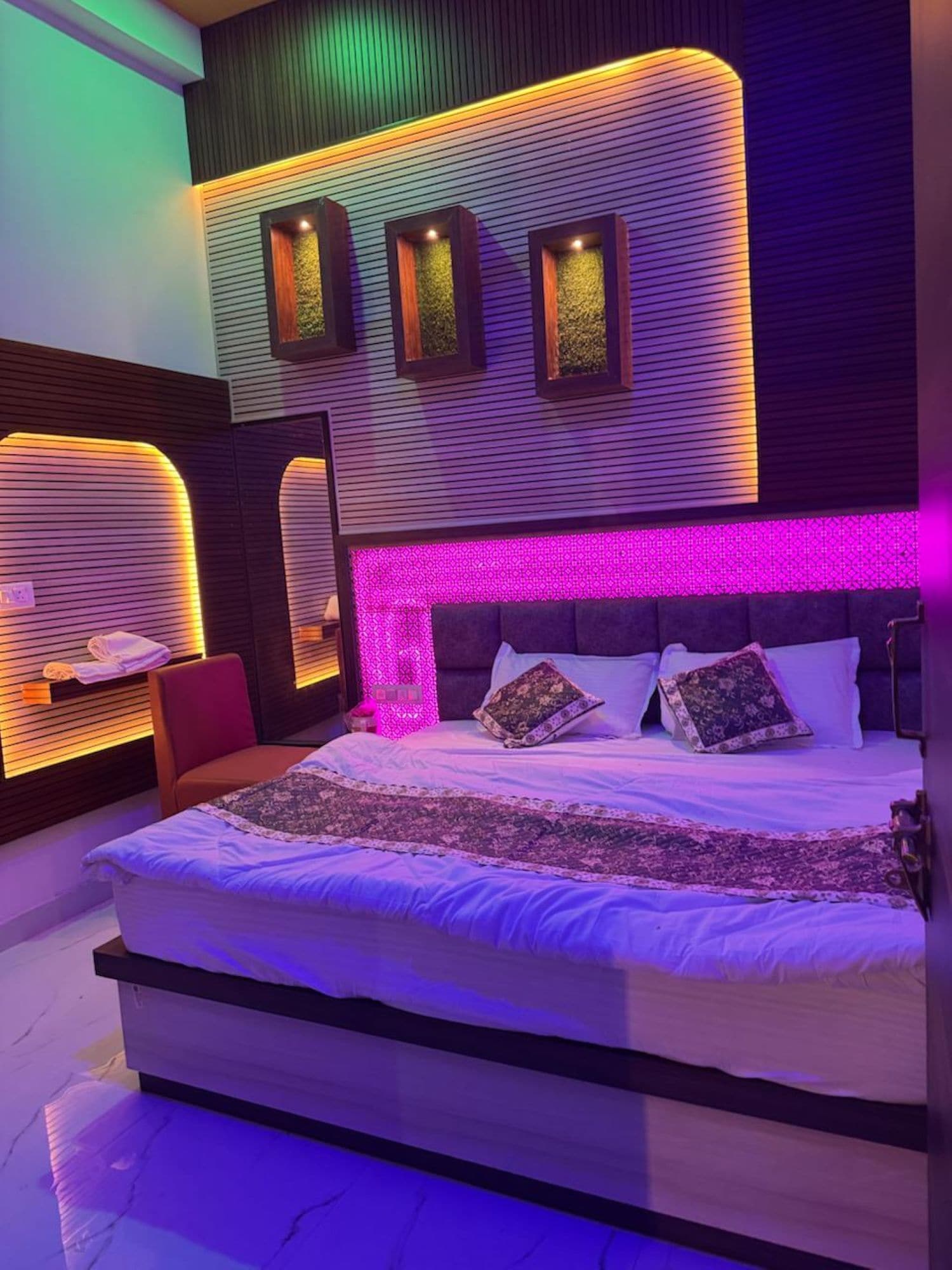 A modern bedroom with a large bed, a headboard with built-in lighting, and a wall-mounted shelf with towels.