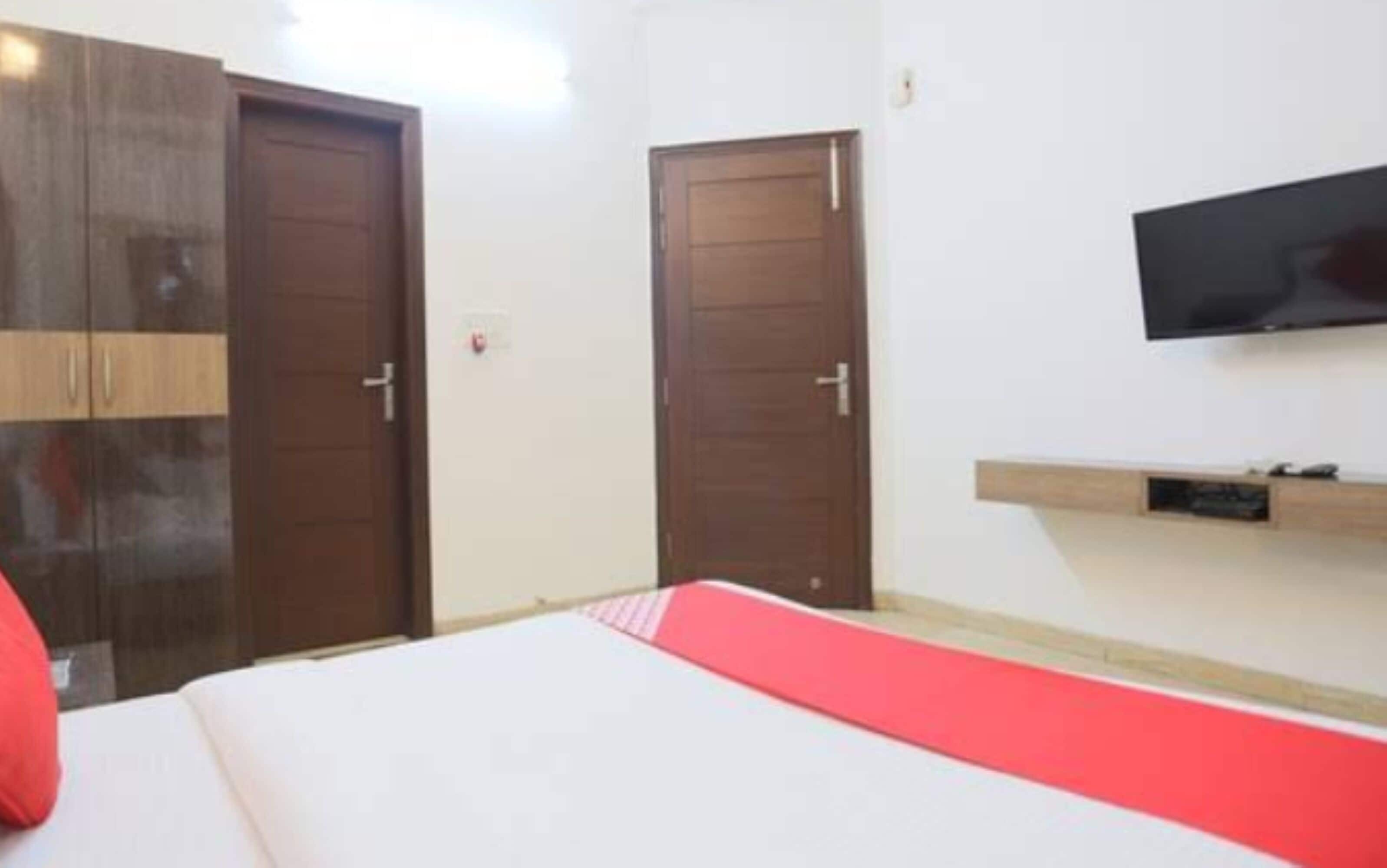 A bedroom with a bed, two wooden doors, a TV mounted on the wall, and a small shelf.