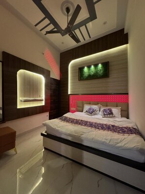 A modern bedroom with a large bed, a ceiling fan, a wall-mounted TV, and a unique lighting design. - Sanwariya Guest House And Resort (Danta Ramgarh)