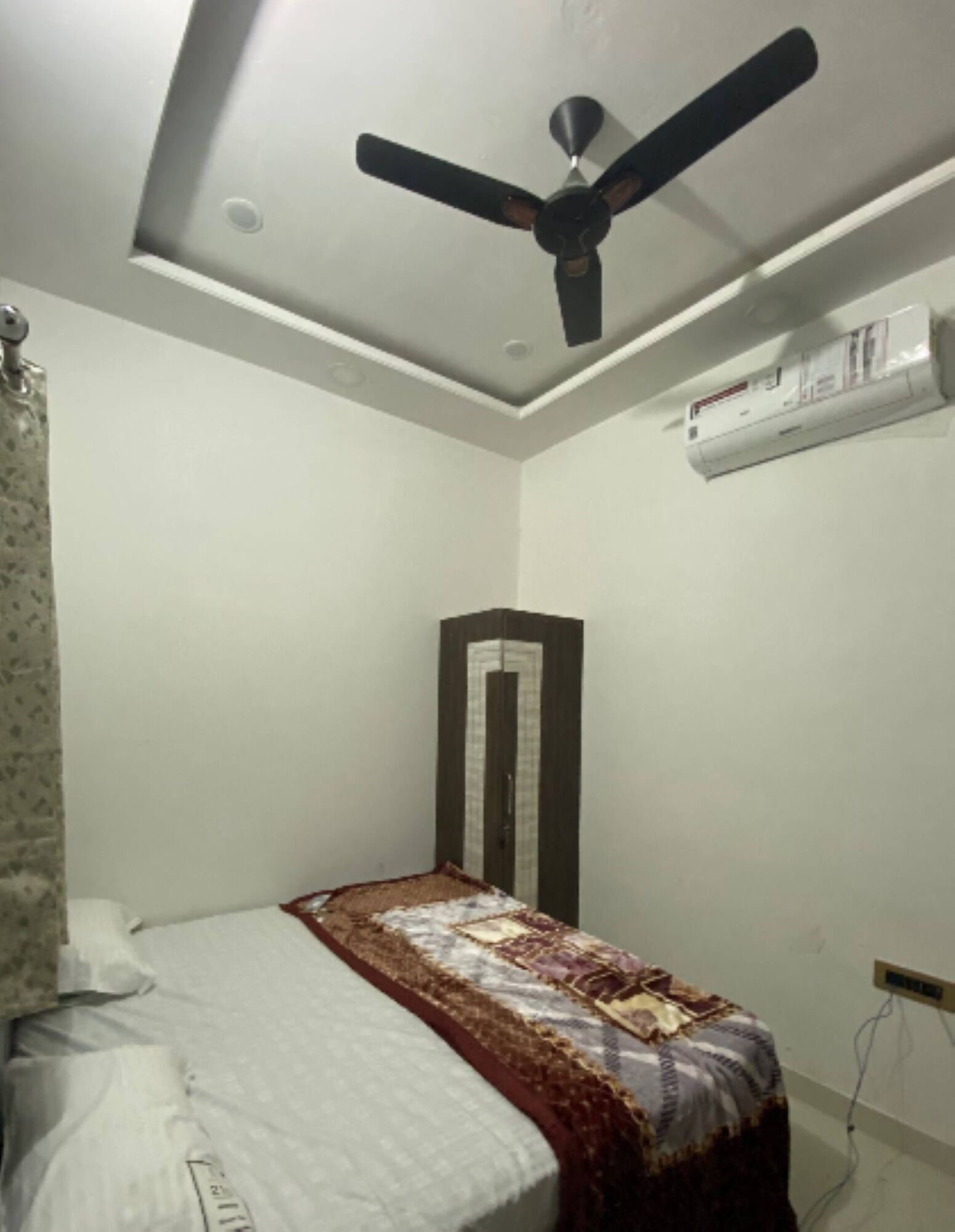 A bedroom with a bed, a ceiling fan, an air conditioning unit, and a wardrobe.