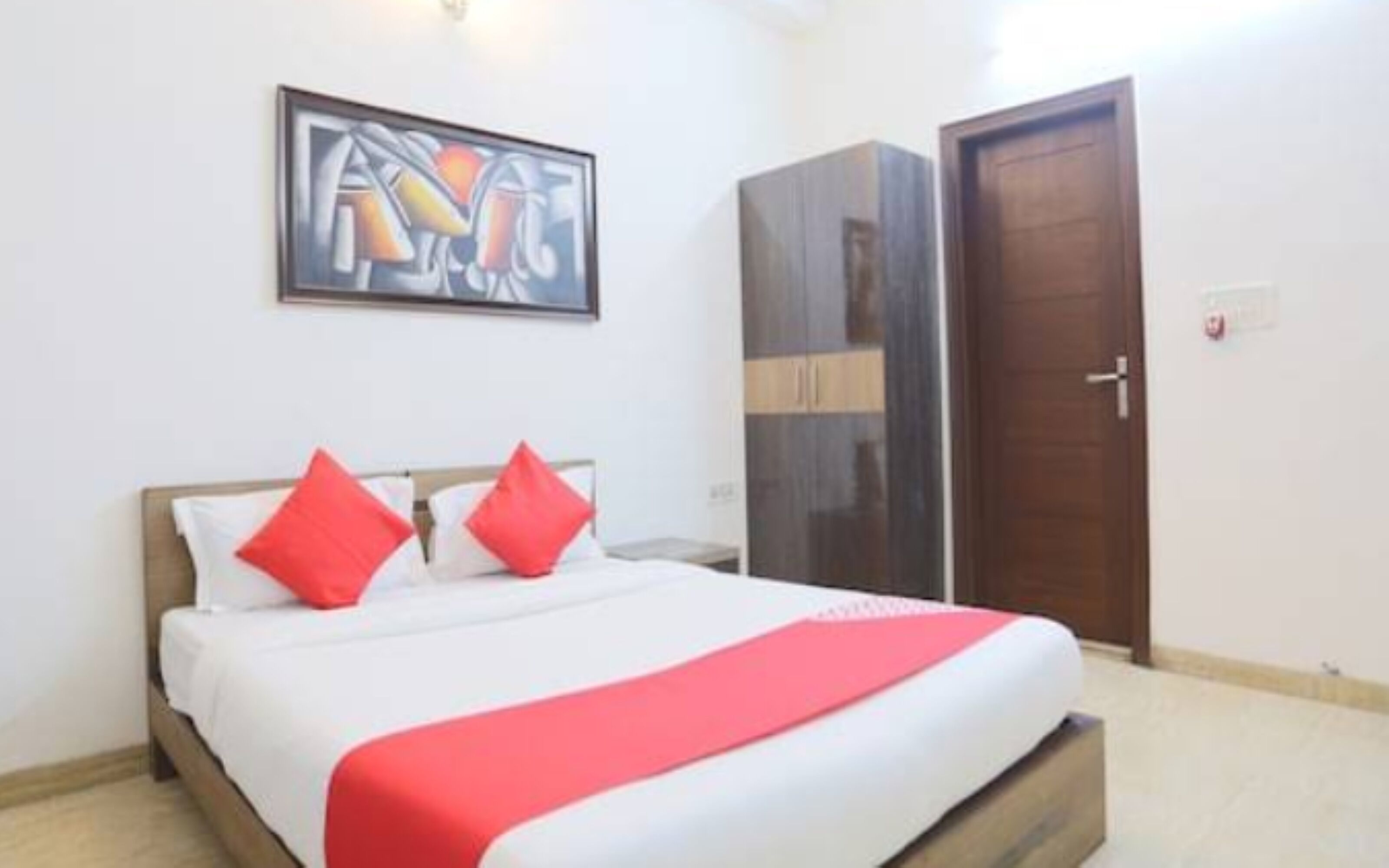 A bedroom with a bed, pillows, a red blanket, a door, and a painting on the wall.