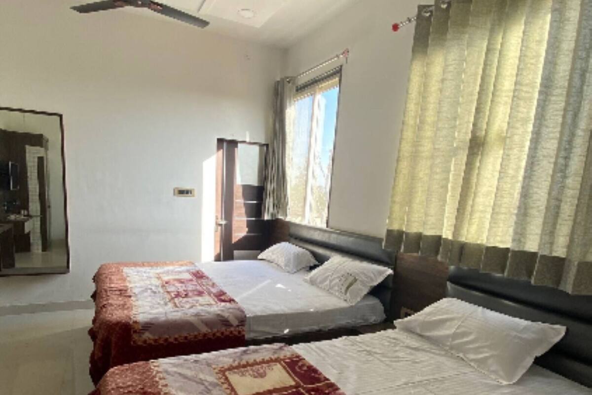 Une chambre avec deux lits, un ventilateur de plafond, une fenêtre avec des rideaux et un miroir au mur.