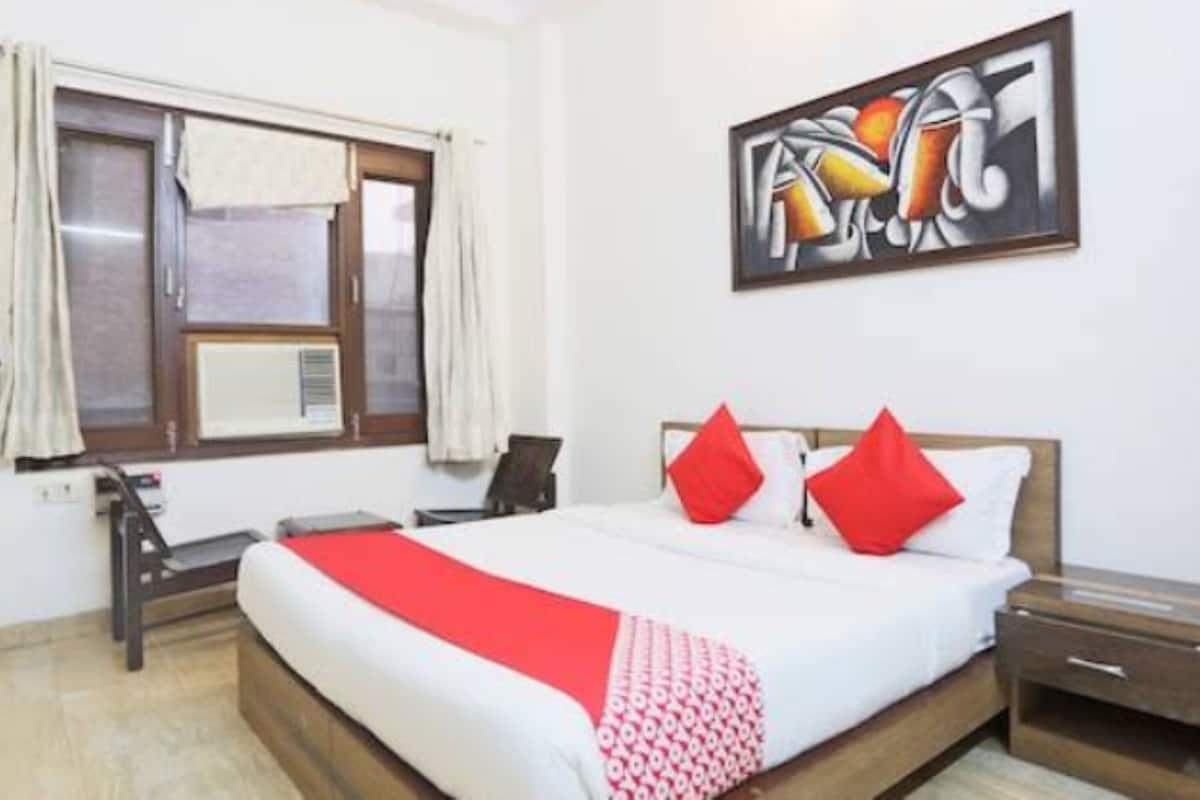 Une chambre d’hôtel avec un lit, une table de chevet, un bureau et une fenêtre avec des rideaux.