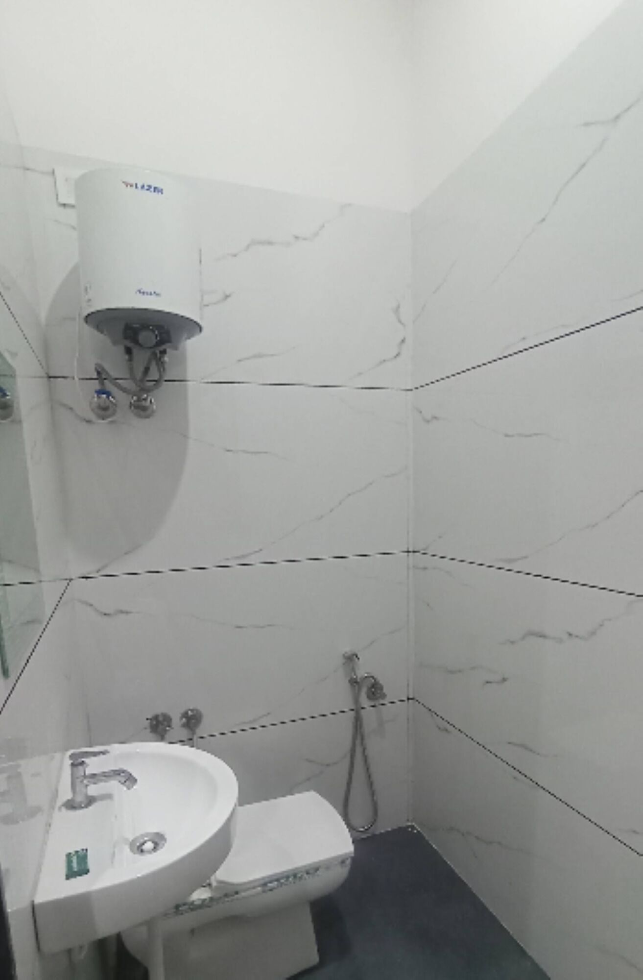 A bathroom with white marble tiles, a white sink, a toilet, and a shower.