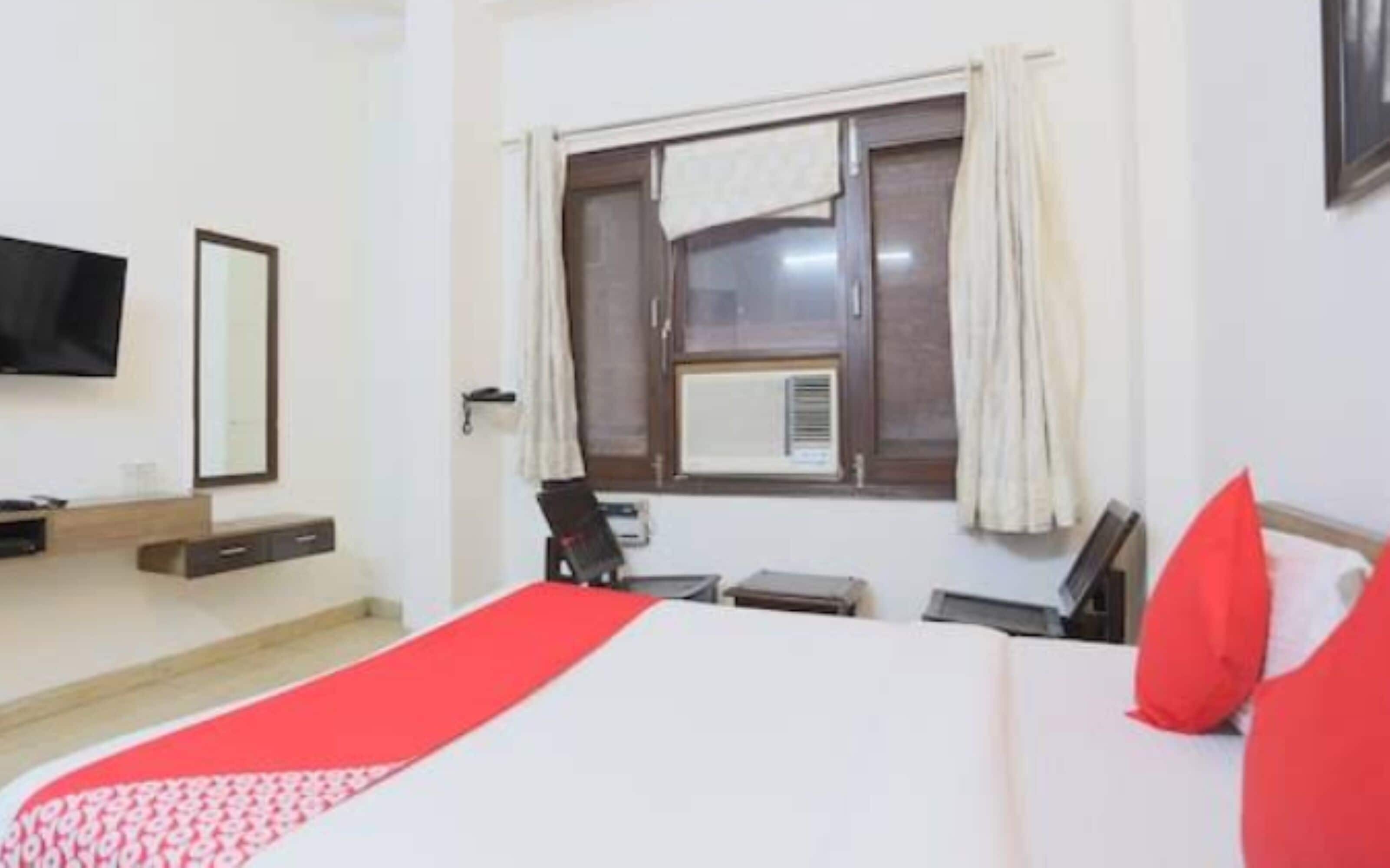 Una camera d'albergo con un letto, una TV fissata al muro, una finestra con tende e un tavolino con una sedia.