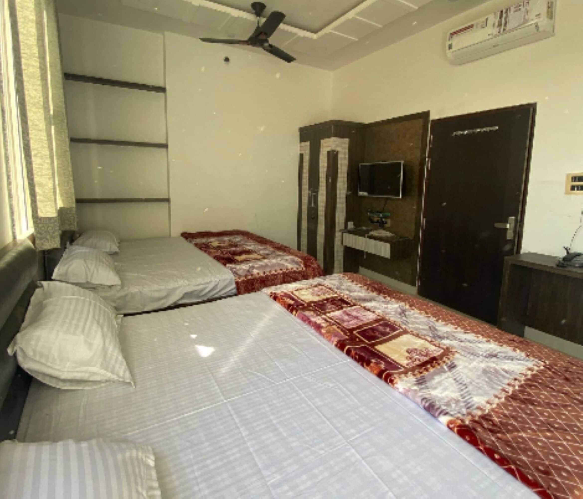 A bedroom with two beds, a ceiling fan, a TV, and a wardrobe.