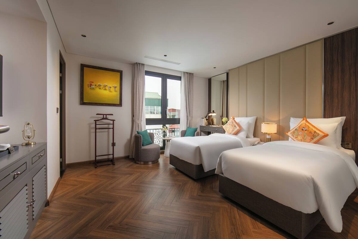 A hotel room with two beds, a desk, a chair, a dresser, and a large window.