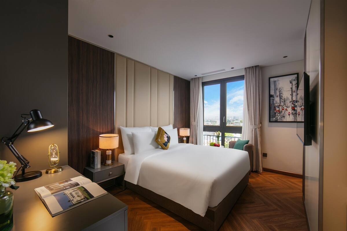 A hotel room with a large bed, bedside lamps, a nightstand, a window with curtains, and a framed picture on the wall.