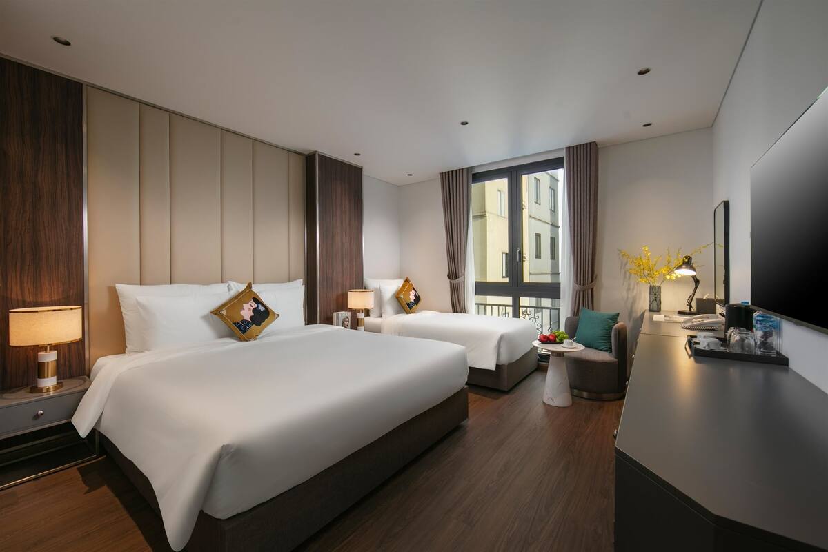 A hotel room with two beds, a desk, a chair, a TV, and a window with curtains.