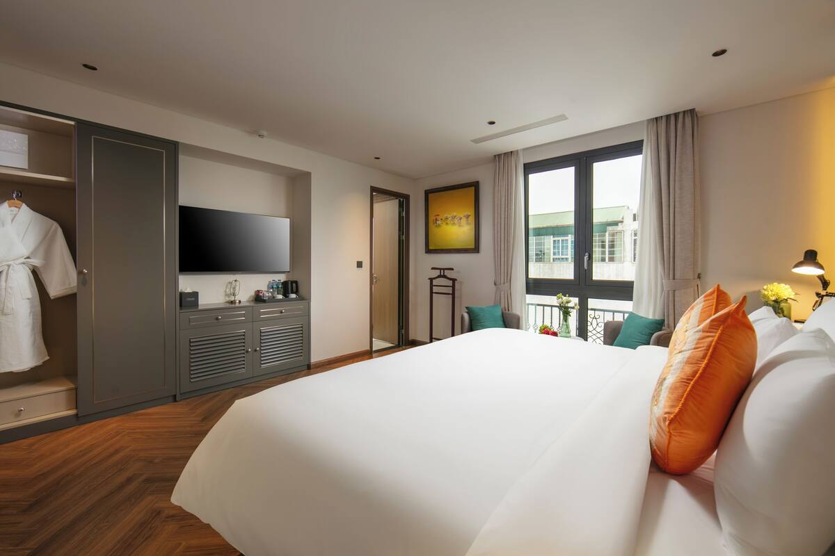 A hotel room with a large bed, a wardrobe, a flat-screen TV, a balcony with a view, and a desk with a lamp.