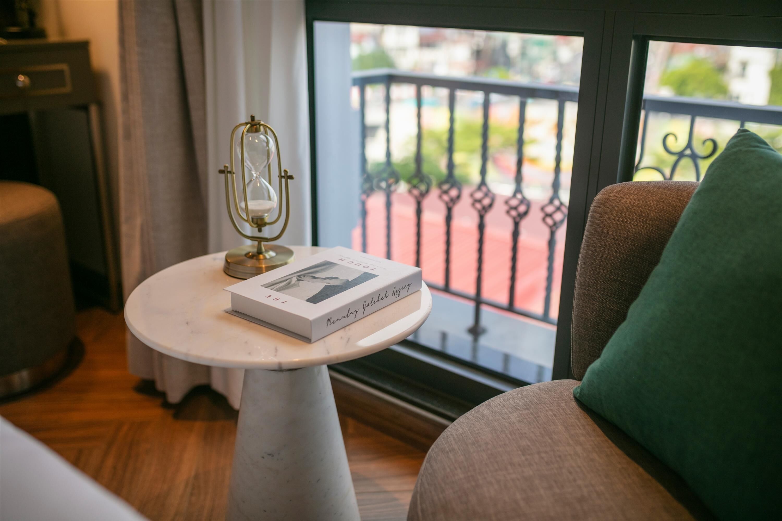 Ein Zimmer mit einem runden weißen Tisch, einem Buch mit dem Titel 'Memories of a German Girl' und einem grünen Kissen auf einem braunen Stuhl.